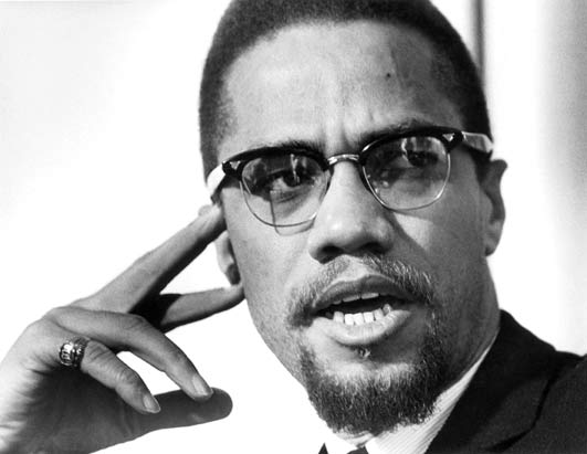 Malcolm X rests two fingers to his head and glances off to the side in this black and white photo.