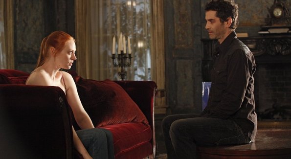 A young redheaded vampire, Jessica, looks on with fear and trepidation as an mean older vampire, Franklin, questions her in her living room.  A scene from the latest episode of True Blood.