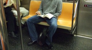 Photo of a man taking up two subway seats by sitting with his legs spread. 
