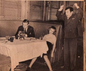Old photo of a man at a dinner table, a woman passed out at the table, and another man throwing his hands up in frustration. 