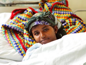 A young fistula patient lays in bed. She is looking at the camera and smiling slightly. 