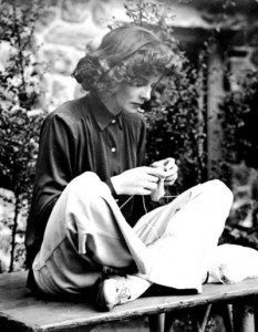 Katharine Hepburn sits cross-legged on a bench knitting (on the set of Bringing Up Baby)