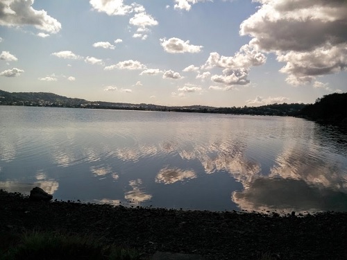 A blue sky with scattered fluffy clouds reflected in the waters of a lake