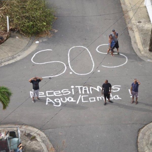 Aerial shot of people in Humacao, Puerto Rico, next to the words "S.O.S. Necesitamos Agua/Comida" written on the street