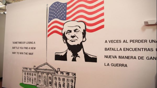 A mural on the wall of a child immigrant detention center with an image of Donald Trump, the White House, and the American flag, along with the words "Sometimes by losing a battle you find a new way to win the war" in English and Spanish